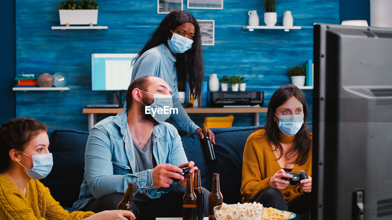 Cheerful people wearing mask while playing video game at home