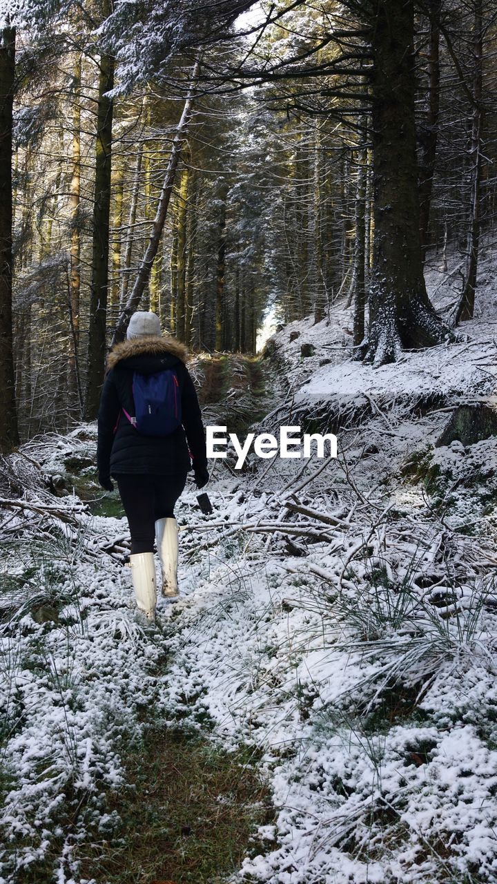 Rear view of woman walking in snow covered forest
