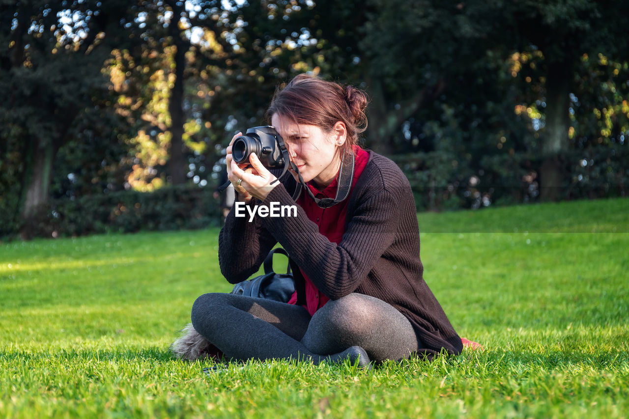 YOUNG MAN PHOTOGRAPHING WHILE SITTING ON GRASS