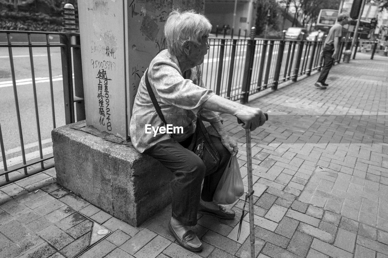 MAN SITTING ON FOOTPATH IN CITY