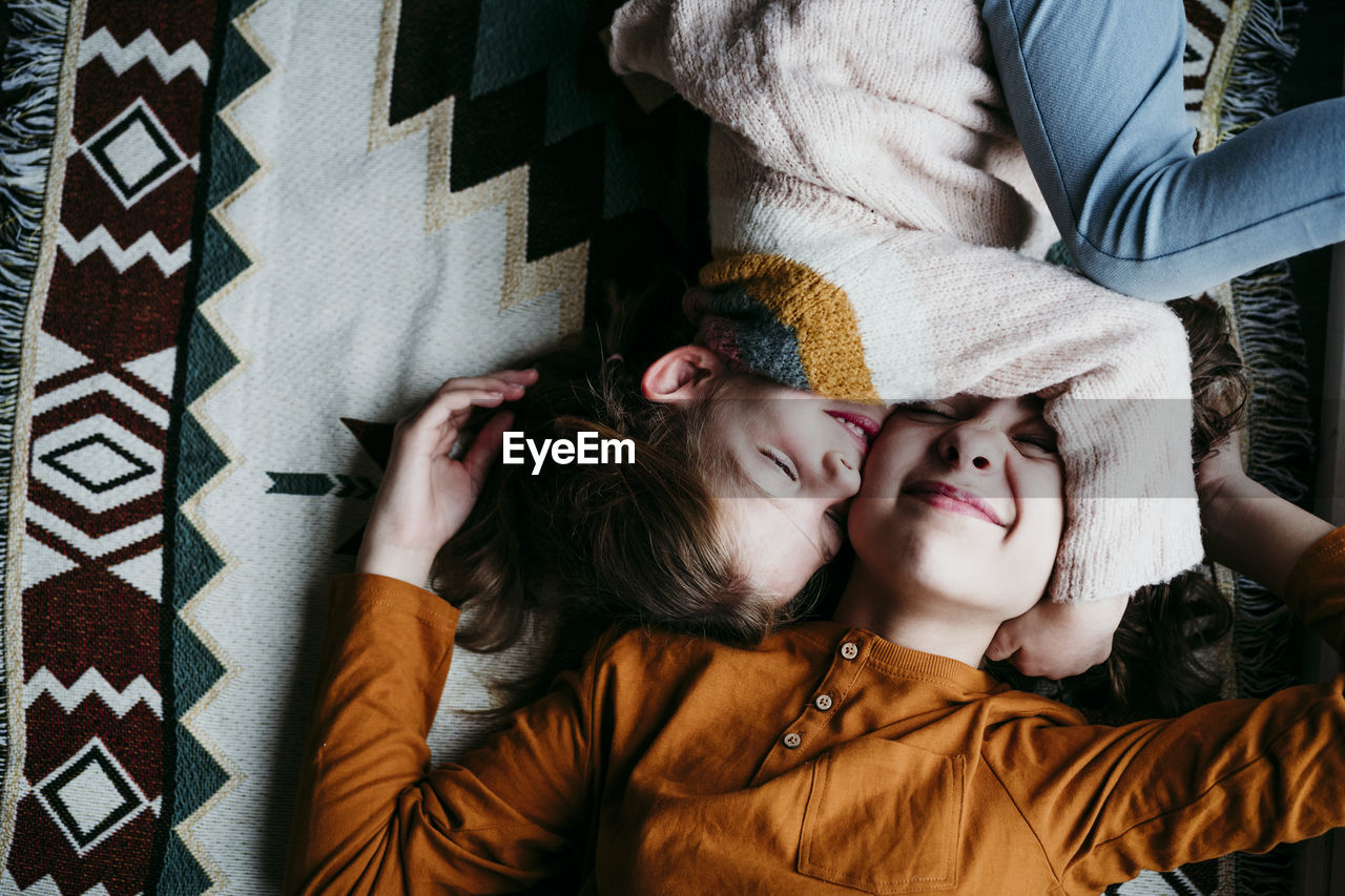 Girl embracing sister face while lying on blanket at home