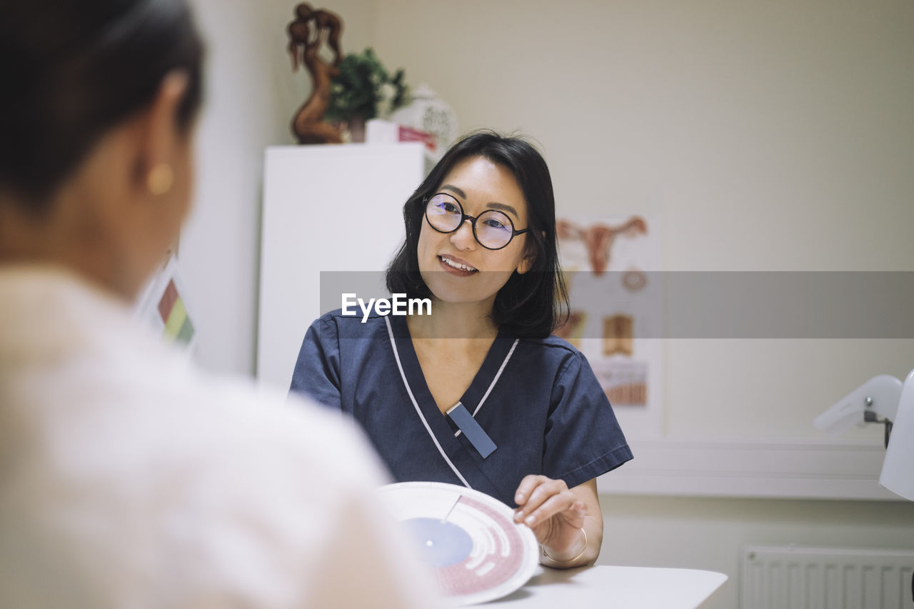 Smiling female healthcare worker showing in vitro fertilization chart while discussing with patient in clinic