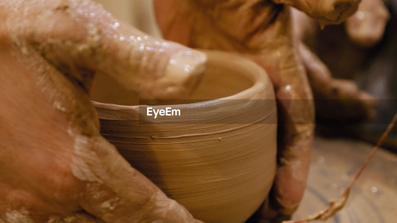 Cropped hands of potter making pot on pottery wheel