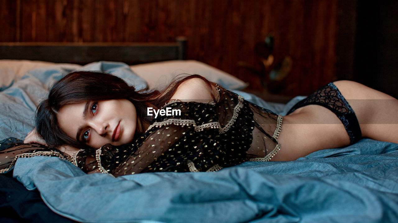 Portrait of sensuous young model wearing lingerie while lying on bed at home