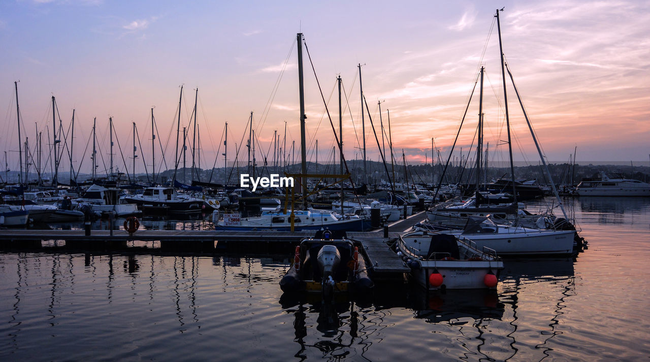 Boats moored in harbor at sunset