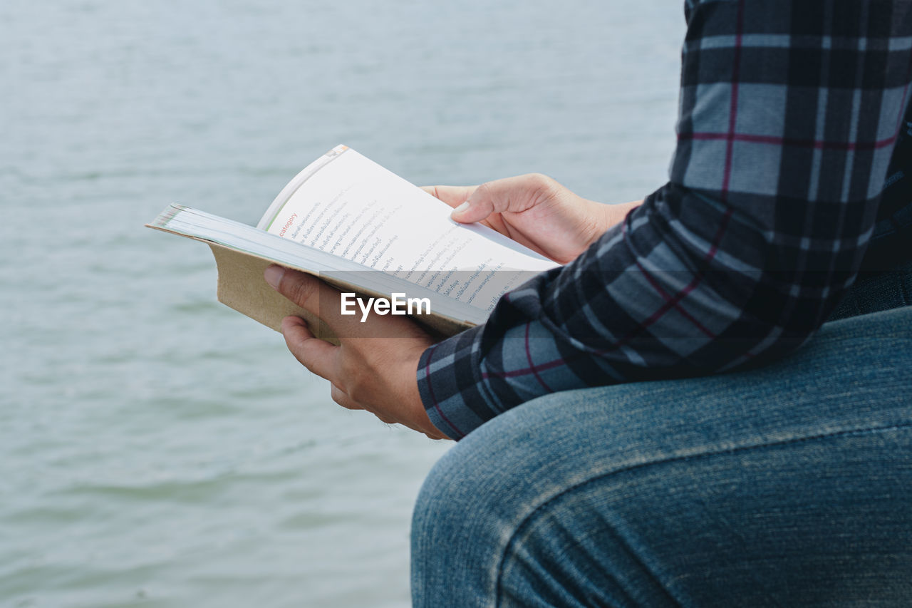 MIDSECTION OF PERSON HOLDING BOOK AGAINST SEA