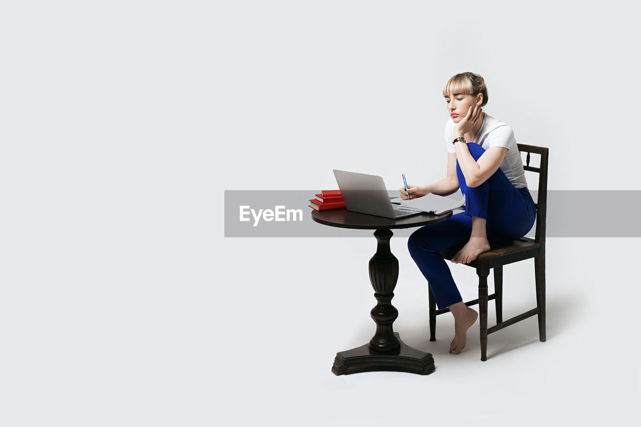 portrait of woman using laptop while sitting on table against white background