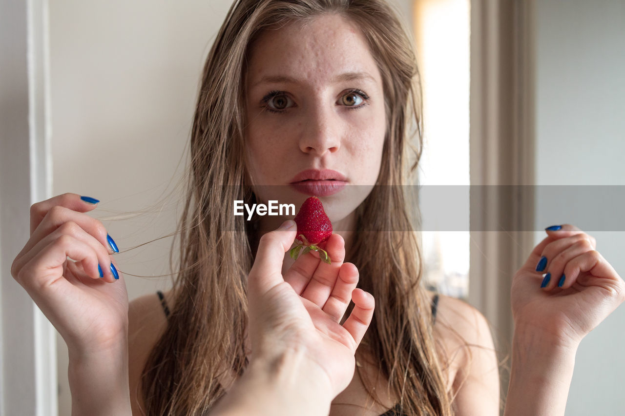 Cropped hand of woman feeding strawberry to friend at home