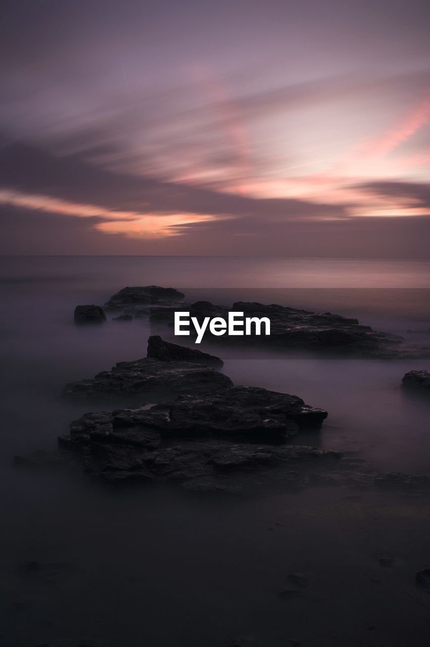 Scenic view of rocks in sea against sky during sunset