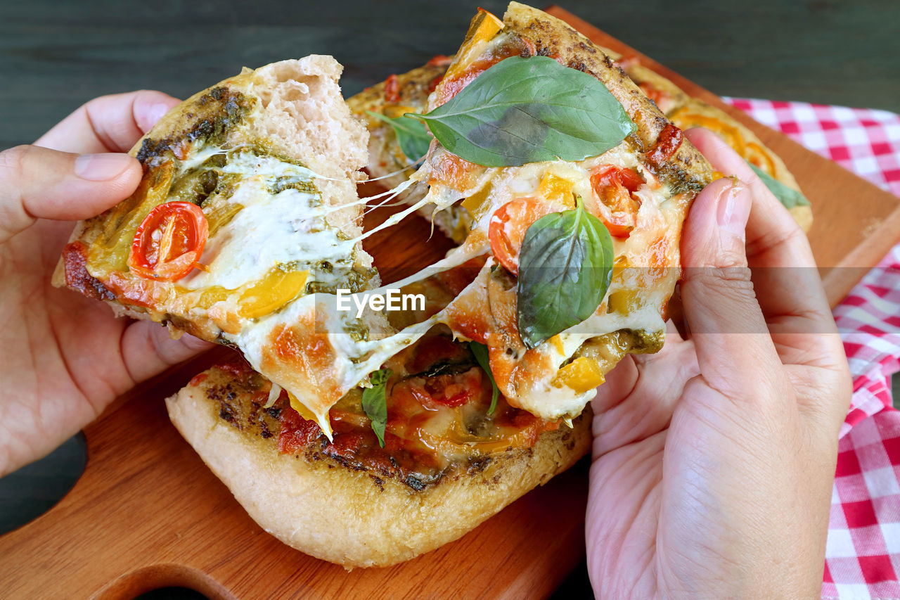 Slices of mouthwatering pesto veggie pizza with stretched melting cheese in hands