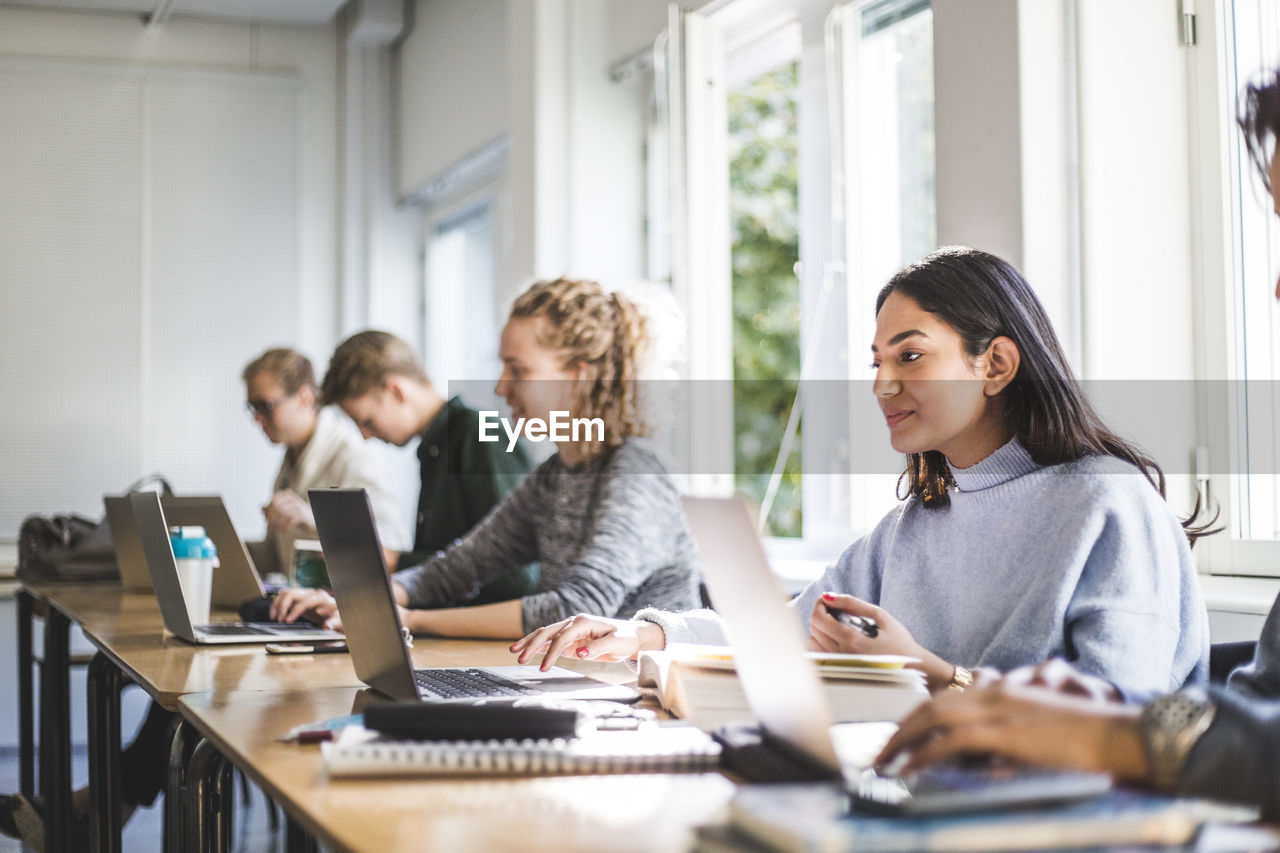 Male and female students using laptops in classroom