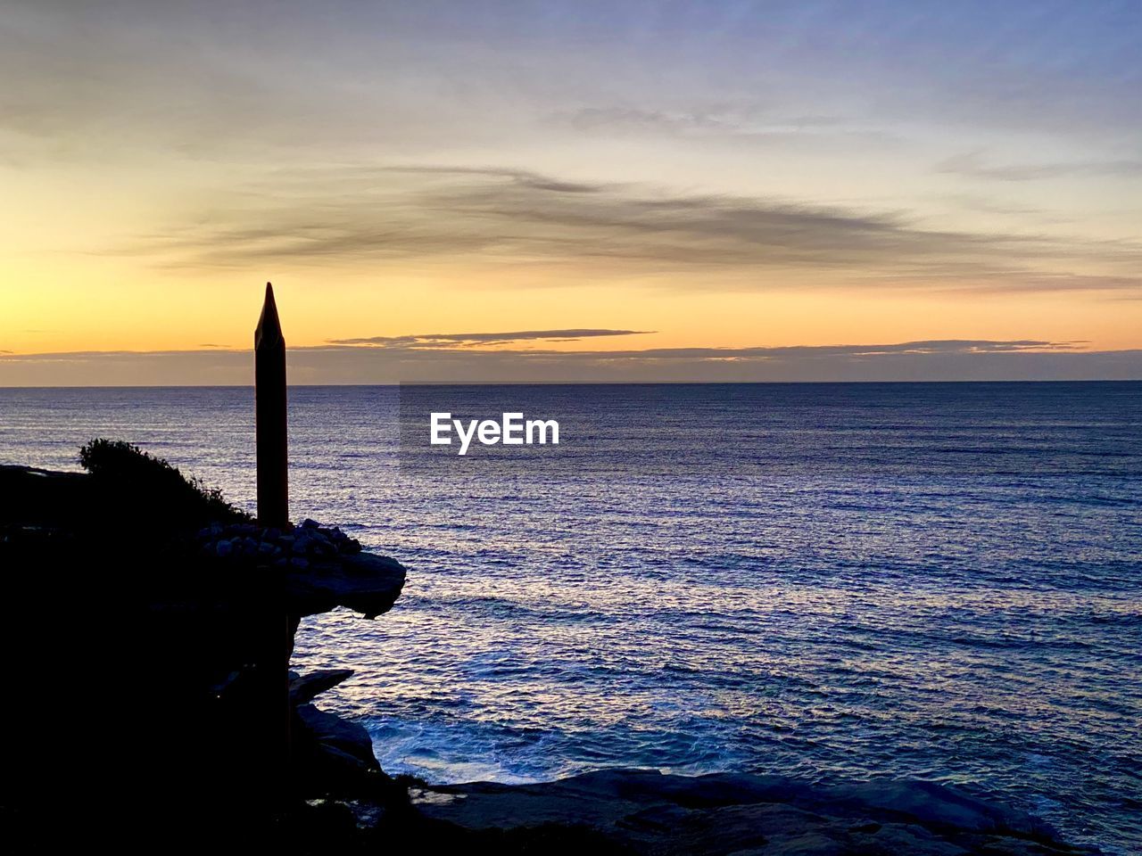 SILHOUETTE WOODEN POSTS ON SEA AGAINST SKY AT SUNSET