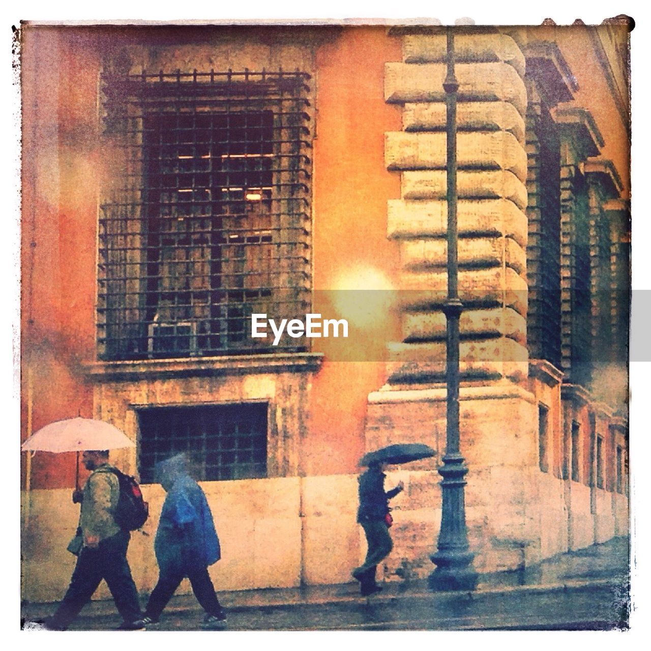 People walking on city street against building during monsoon