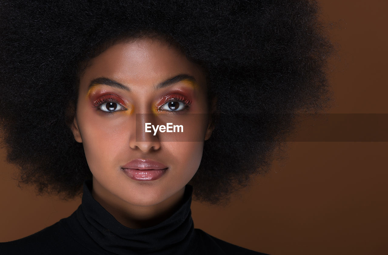 Portrait of beautiful woman with afro hairstyle against brown background