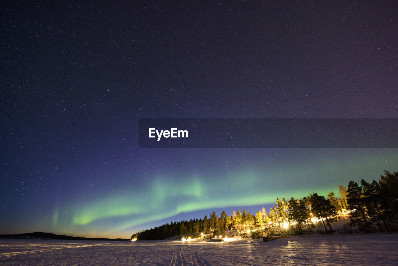 Aurora polaris over landscape against sky at night during winter