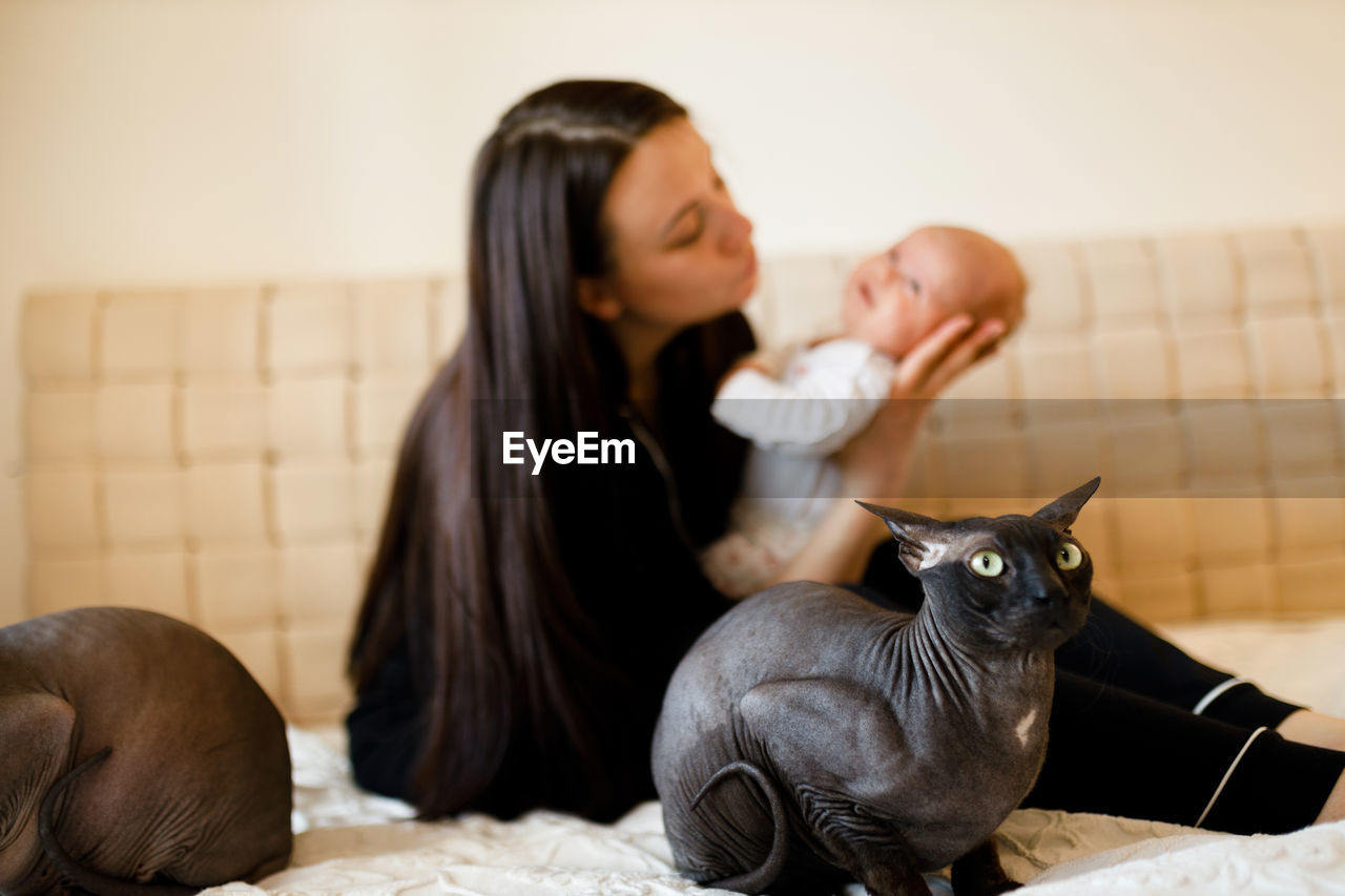 Mother embracing baby while sitting on bed with cats