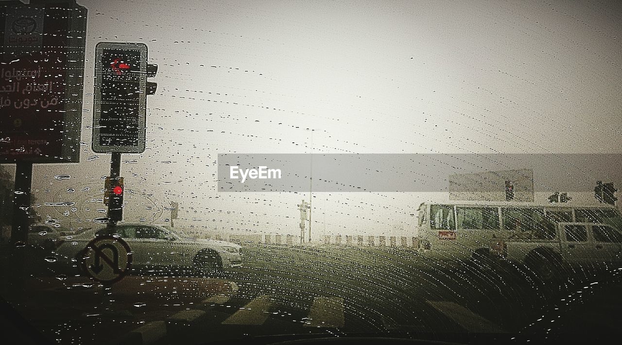 Car and bus against sky seen through wet windshield during monsoon