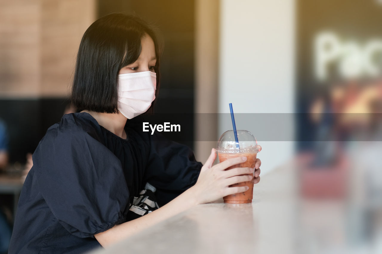 Woman wearing mask while holding drink on table at cafe