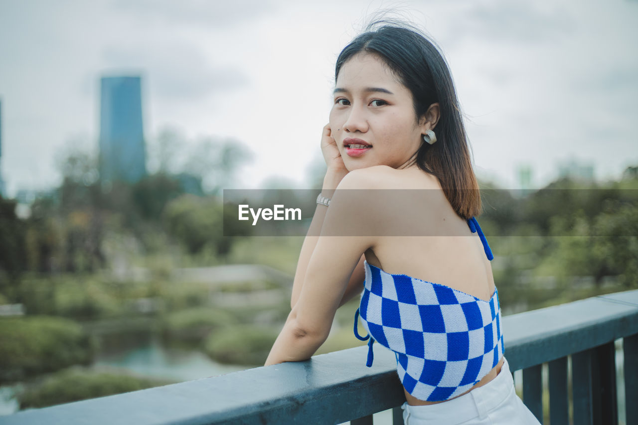 Portrait of young woman standing against railing