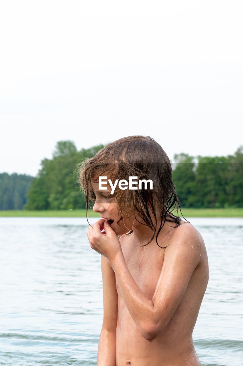 Shirtless boy standing in lake against sky