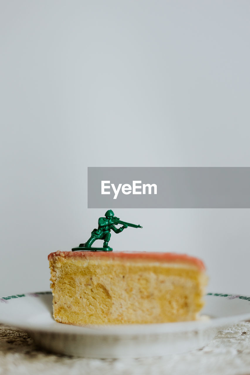 Toy soldier standing on the top of a piece of cake - close up of figurine aginst white background