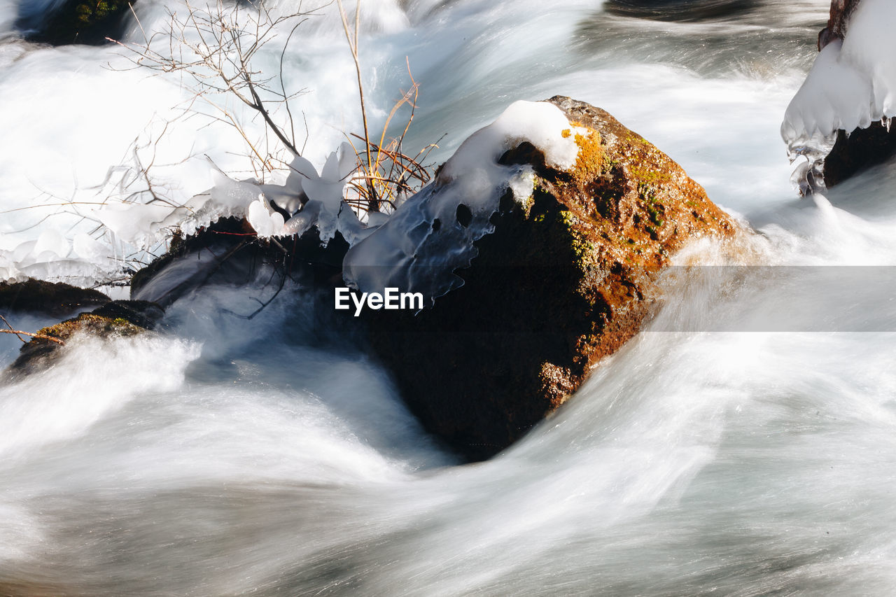 SCENIC VIEW OF WATERFALL BY ROCKS IN WINTER