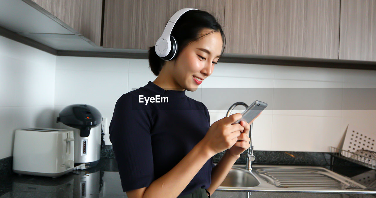 Woman using mobile phone while listening music at home