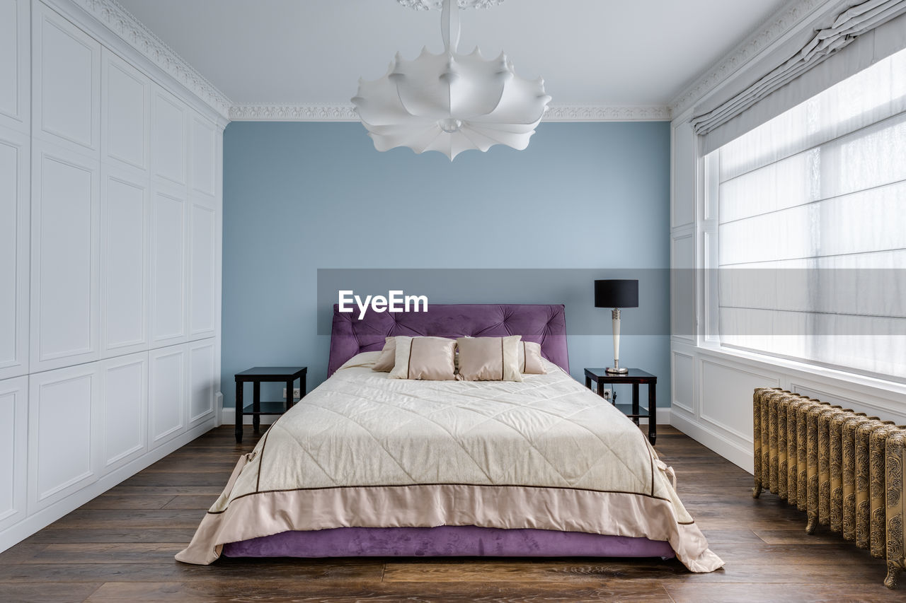 A large purple bed in a blue room near a large window. in the foreground is a glass partition