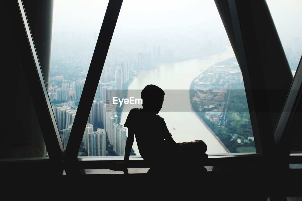 Silhouette of boy sitting against window