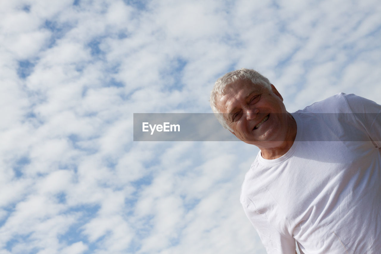 Low angle portrait of mature man against cloudy sky