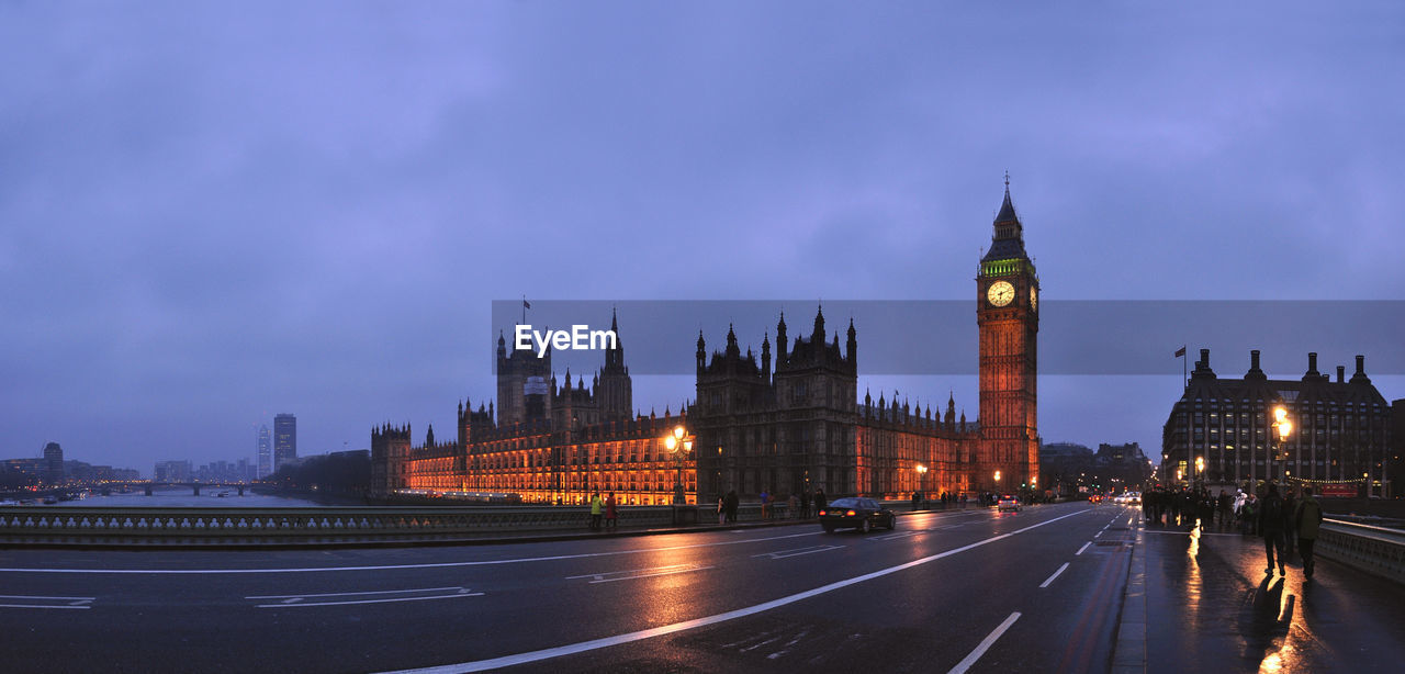 Illuminated big ben by road against cloudy sky at dusk