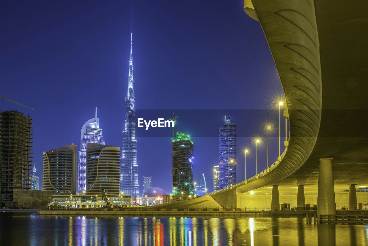 Low angle view of illuminated burj khalifa in front of river in city at night