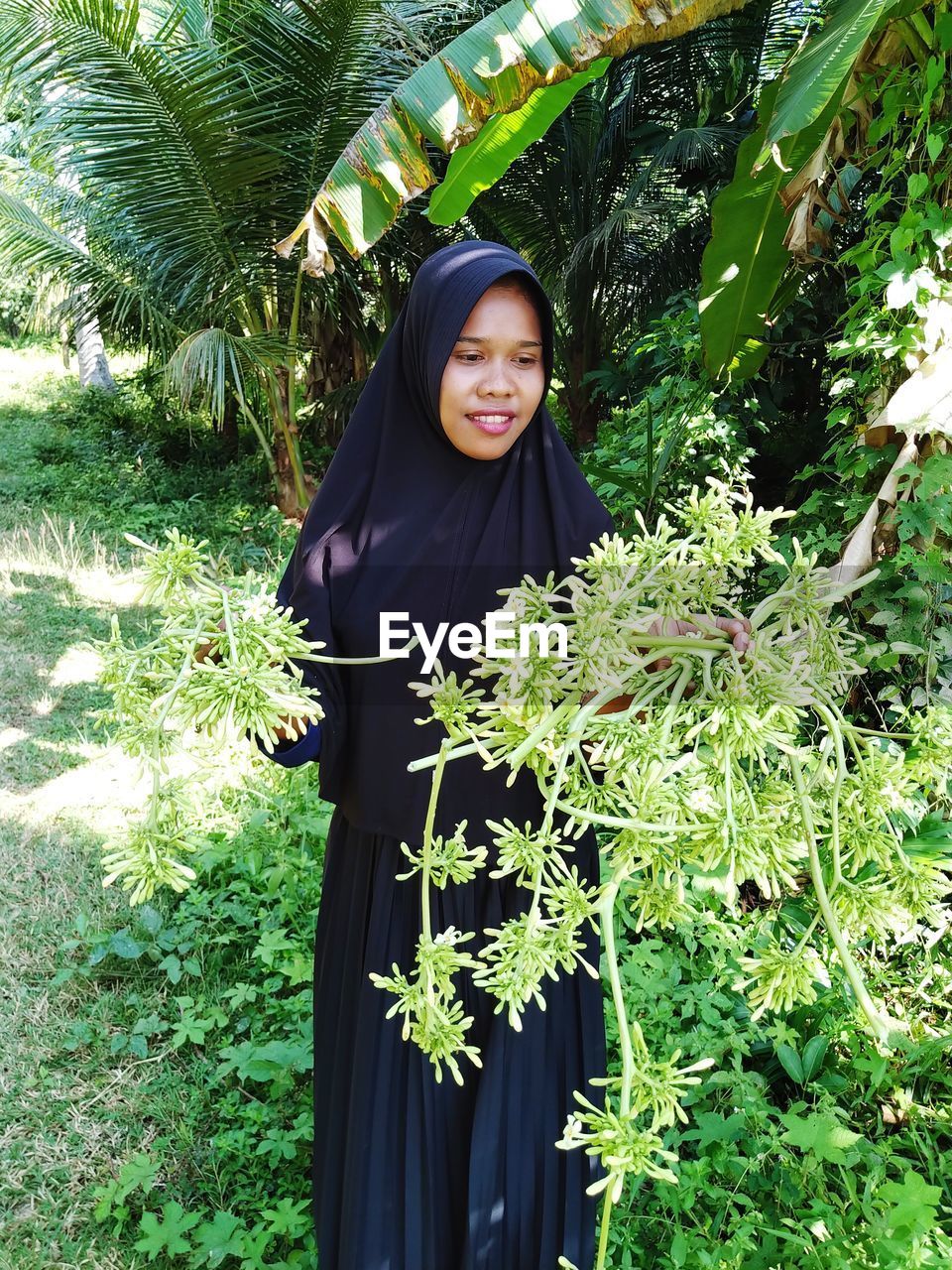 Portrait of smiling young woman standing against plants