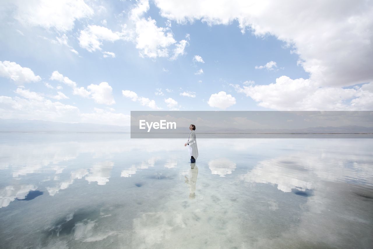 Reflection of cloudy sky and woman on sea