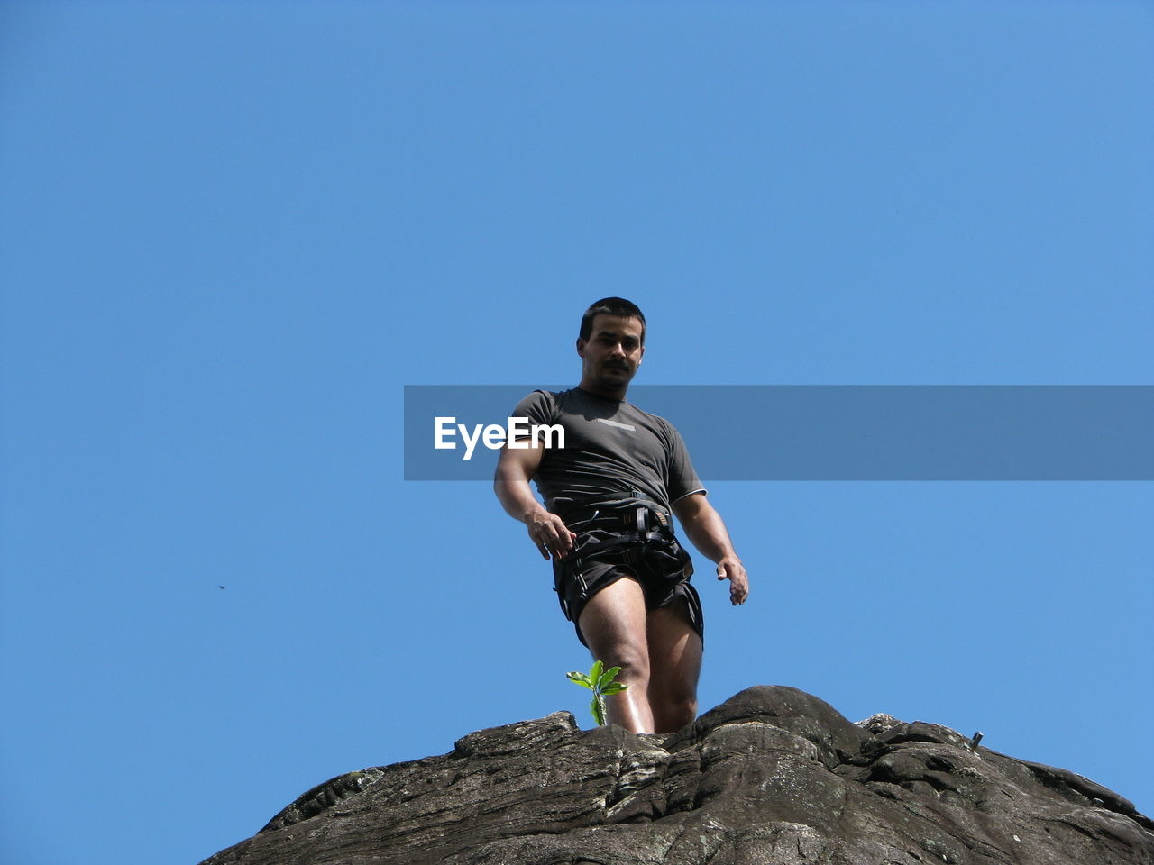 Low angle view of young man standing on rock formation against clear blue sky