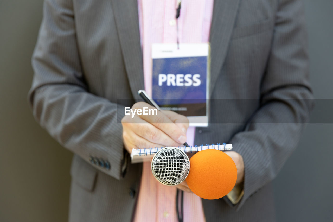 Journalist at press conference or media event, writing notes, holding microphone