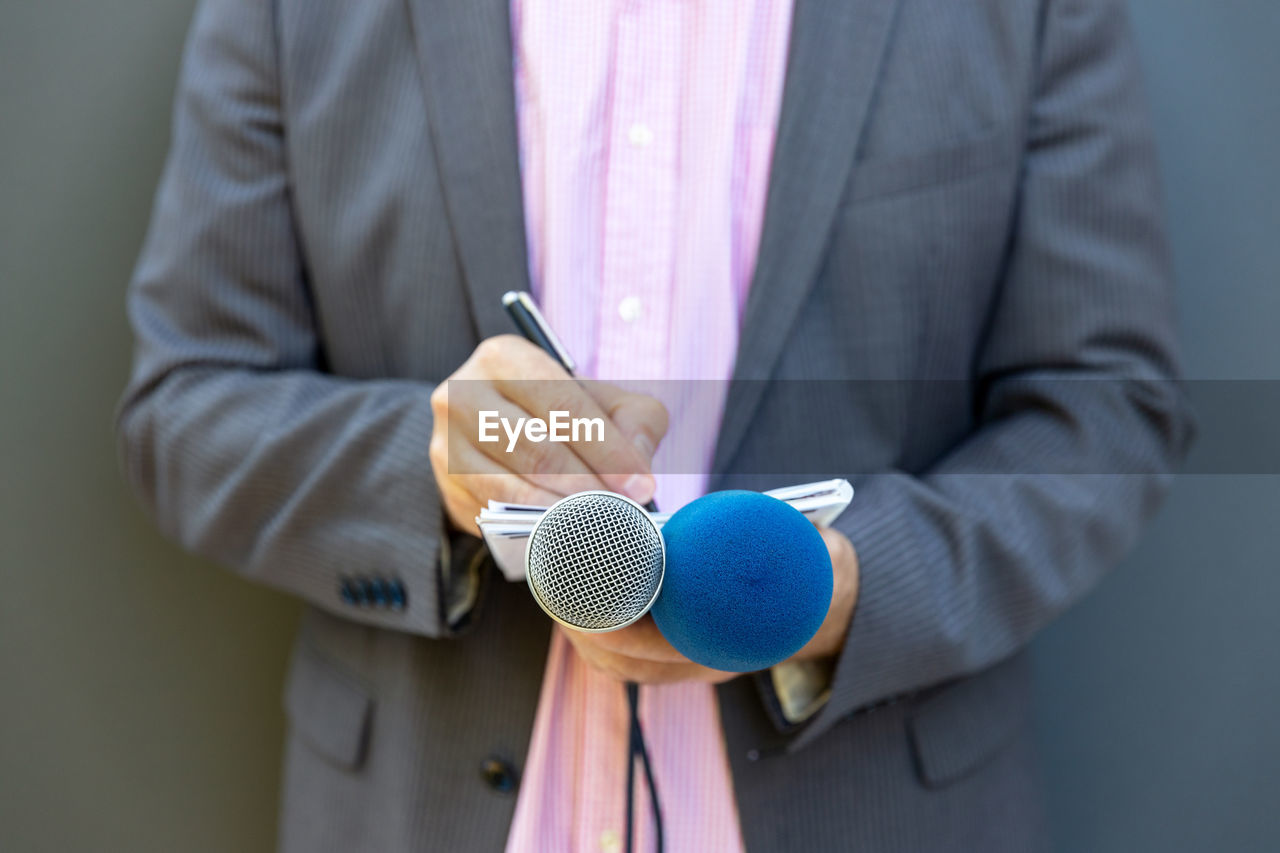 Journalist at press conference or media event, writing notes, holding microphone