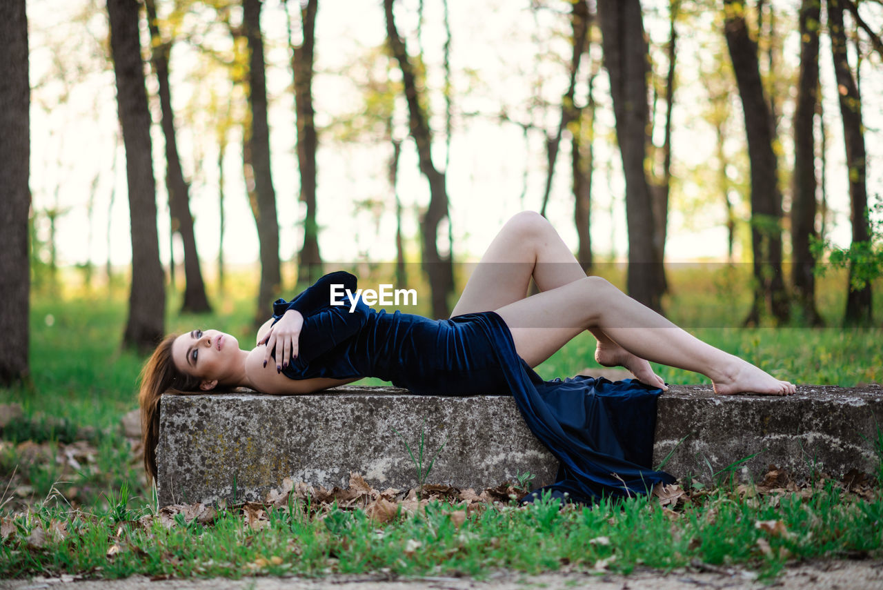 Woman lying down on land against trees in forest