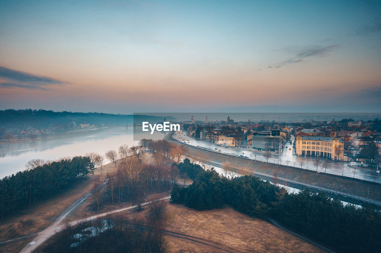 Aerial view of river by buildings in city during sunset