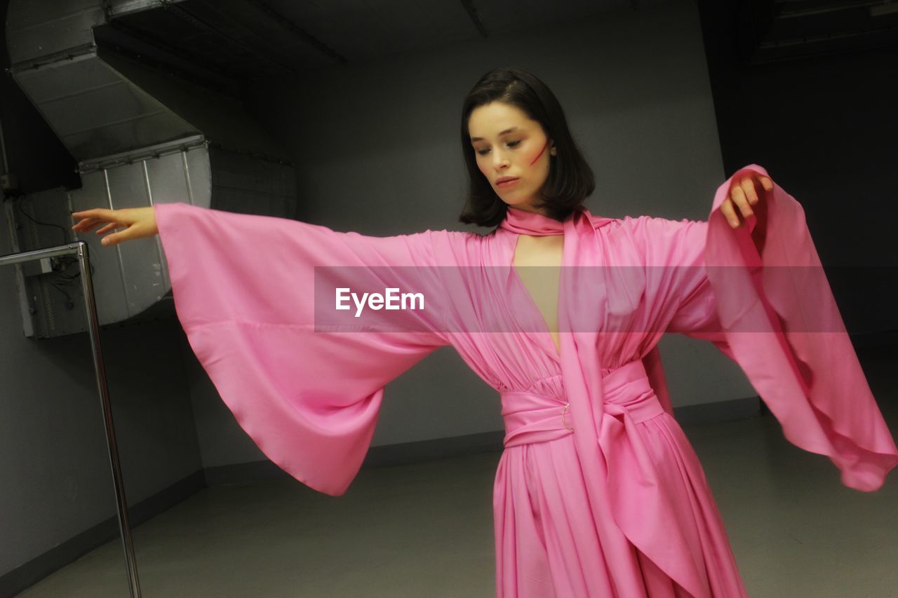 WOMAN HOLDING PINK UMBRELLA STANDING IN CORRIDOR OF BUILDING