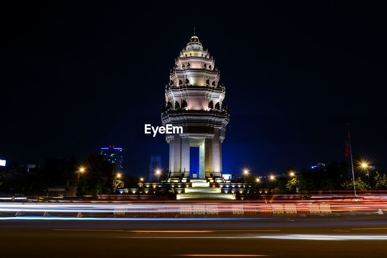 Light trail on city street by illuminated independence monument against sky