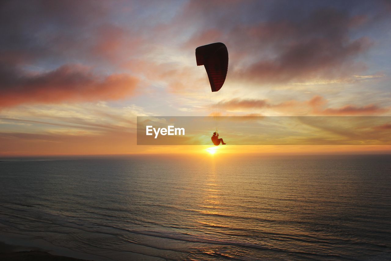 Scenic view of person paragliding during sunset over sea