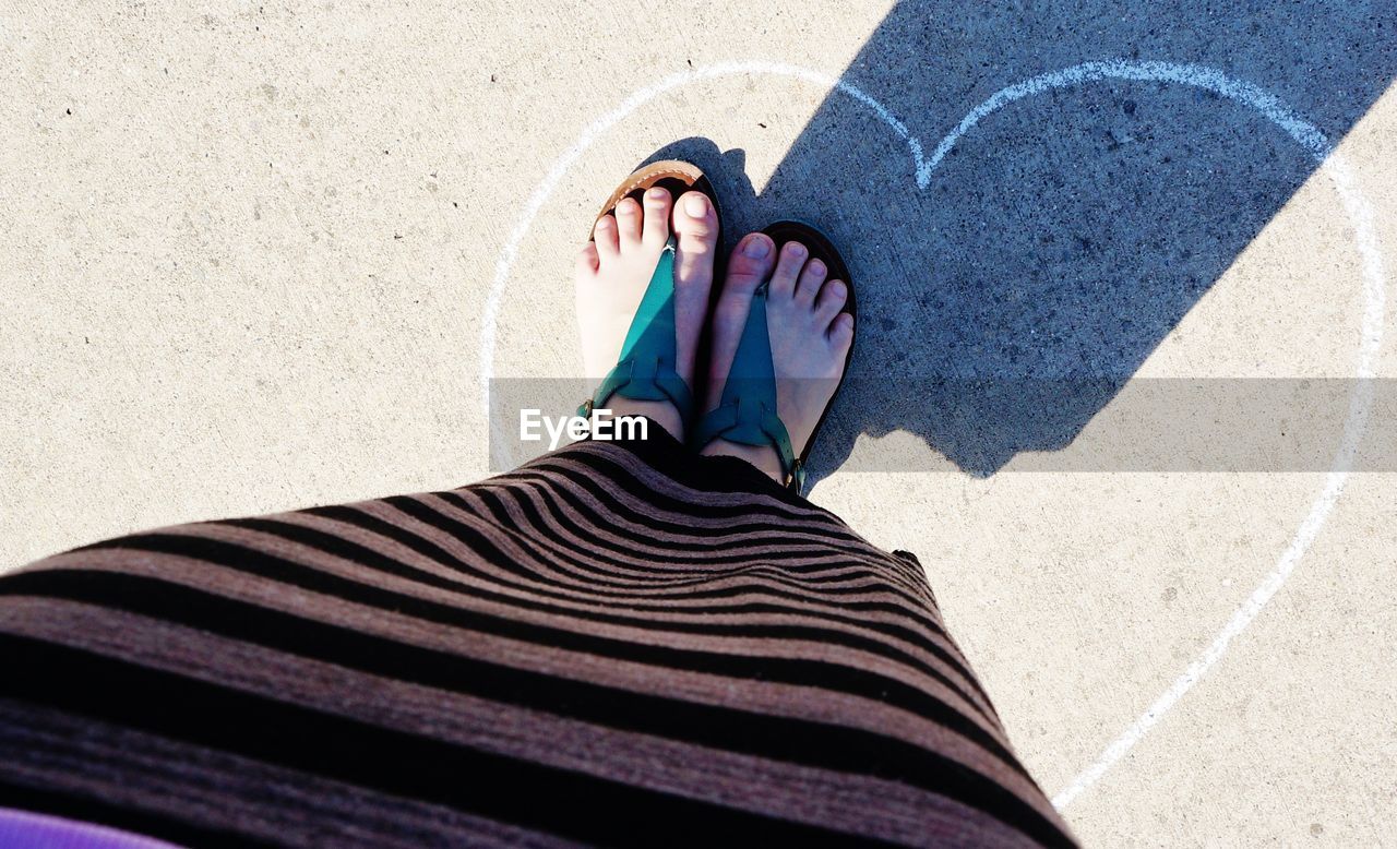 Low section of woman standing on heart shape drawing on footpath