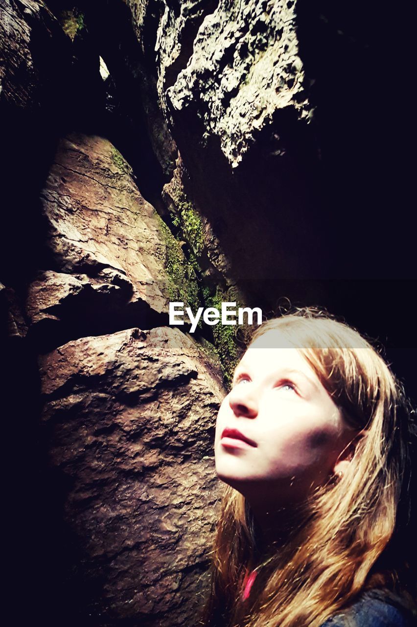 Sunlight falling on girl looking up while standing in cave