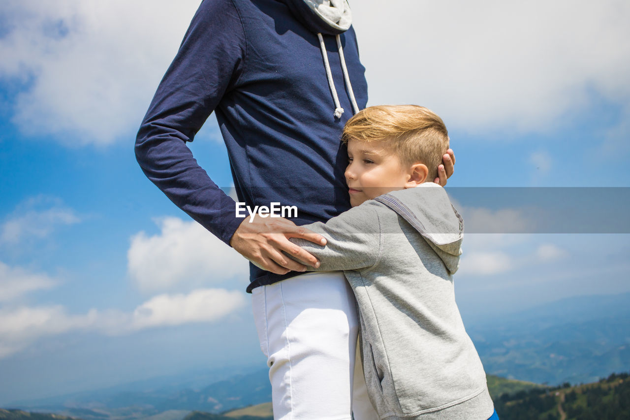 Son embracing father standing against sky
