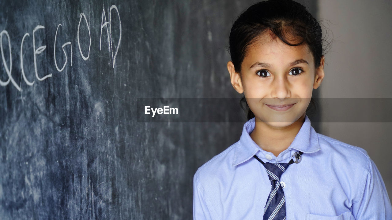 Happy indian school girl child standing in front of black chalkboard background. education concept