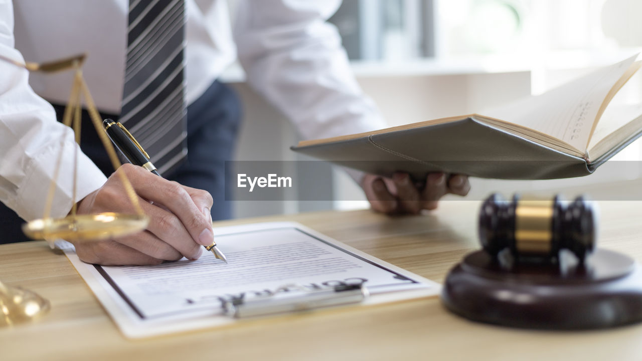 midsection of lawyer writing in book at office