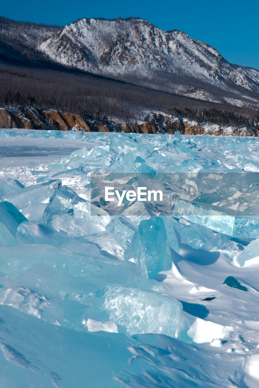 Pieces of crystal clear lake ice with mountains in background