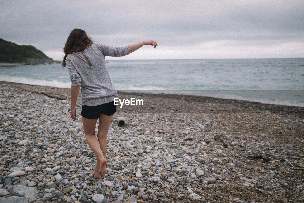 REAR VIEW OF WOMAN STANDING ON BEACH