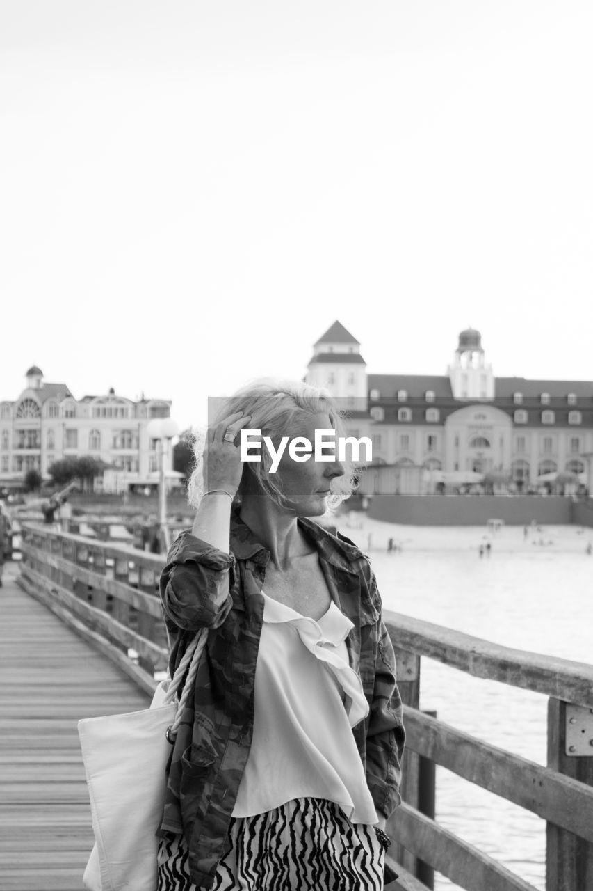 Woman standing by railing in city against clear sky